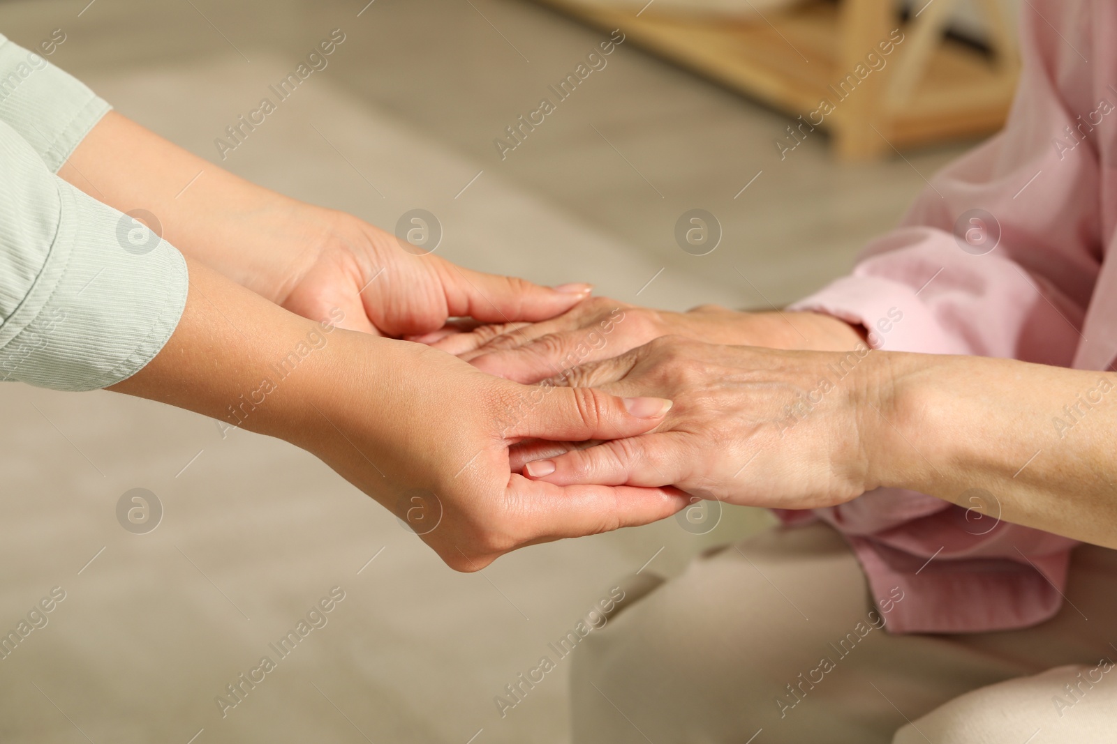 Photo of Young and elderly women holding hands indoors, closeup