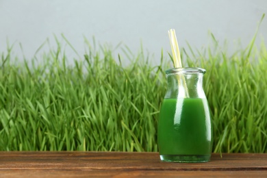 Photo of Bottle of juice and fresh wheat grass on background. Space for text