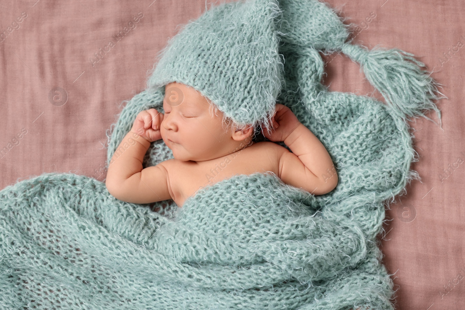 Photo of Adorable newborn baby sleeping under knitted plaid on bed, top view