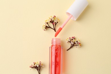 Bright lip gloss, applicator and flowers on yellow background, top view