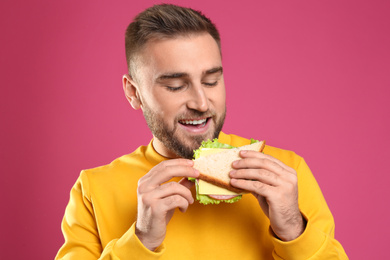 Young man eating tasty sandwich on pink background