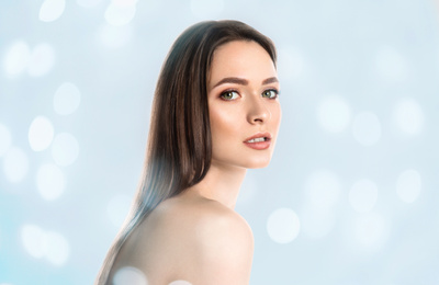 Young woman with perfect smooth skin on light blue background, bokeh effect