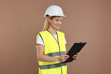 Engineer in hard hat holding clipboard on brown background