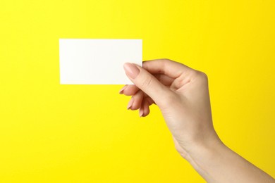 Photo of Woman holding blank business card on yellow background, closeup. Mockup for design
