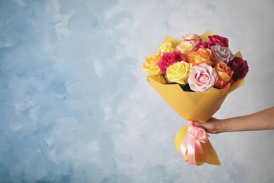 Photo of Woman holding luxury bouquet of fresh roses on light blue background, closeup. Space for text