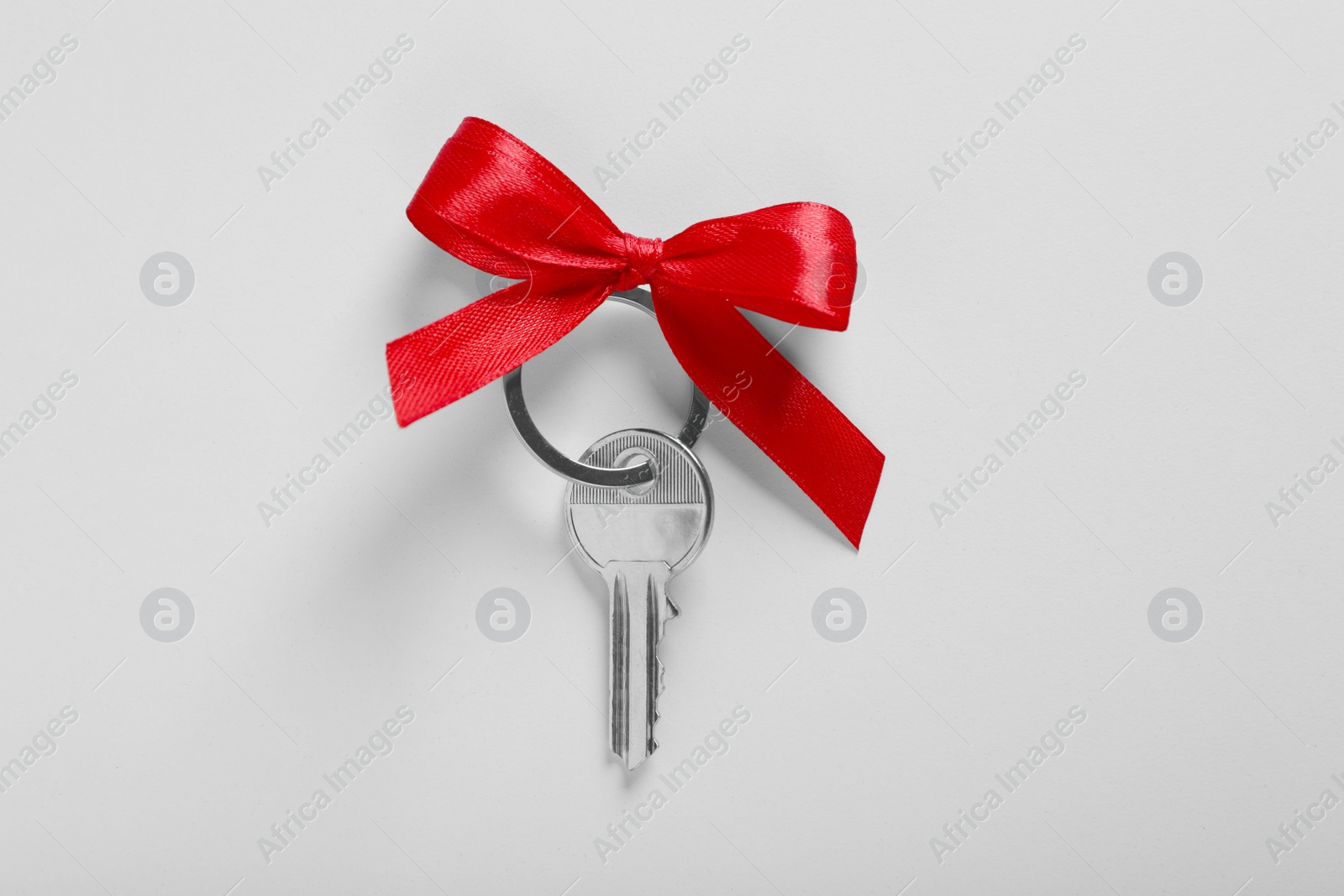 Photo of Key with trinket in shape of house and red bow on light grey background, top view. Housewarming party