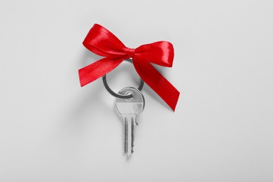 Key with trinket in shape of house and red bow on light grey background, top view. Housewarming party