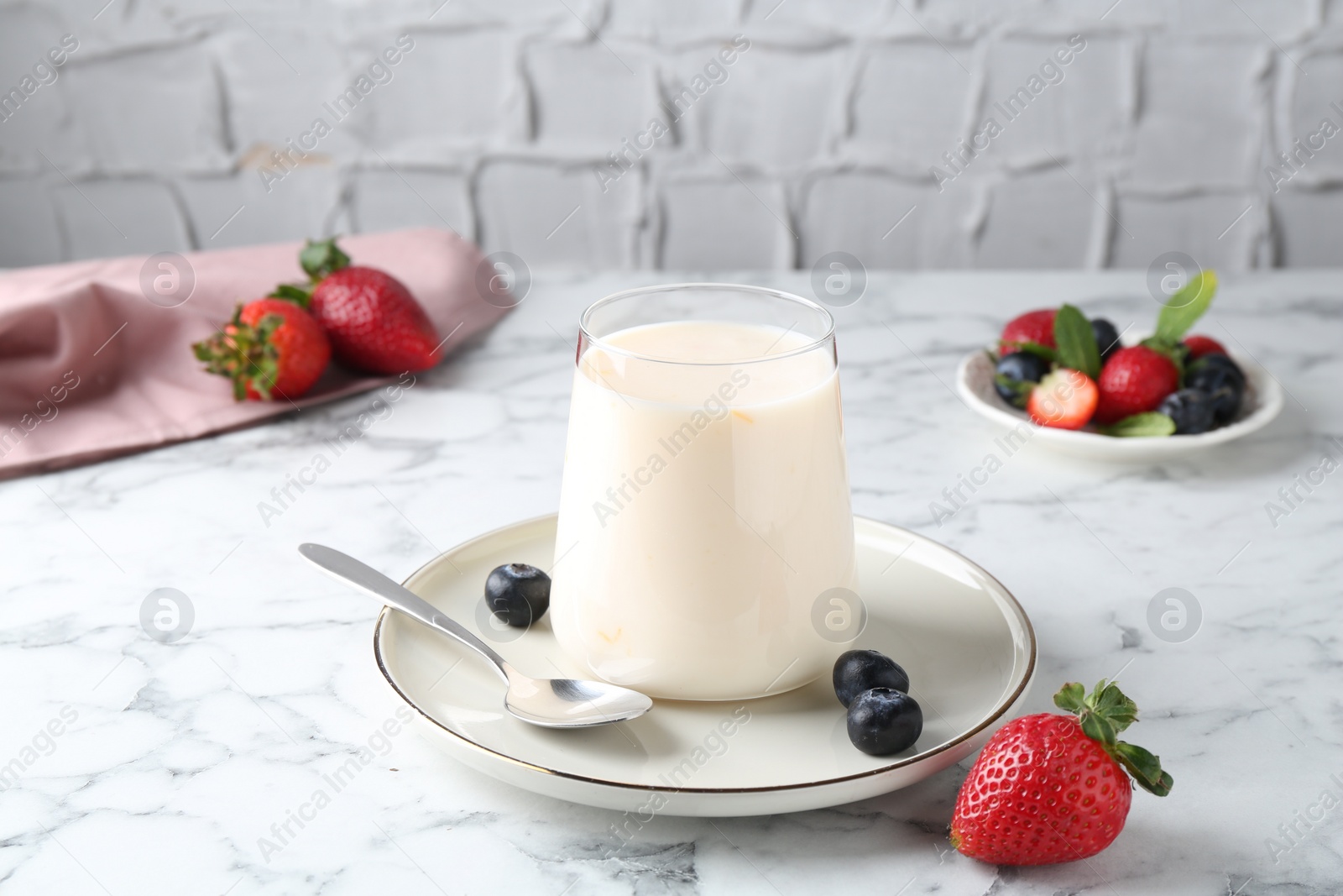 Photo of Tasty yogurt in glass and berries on white marble table