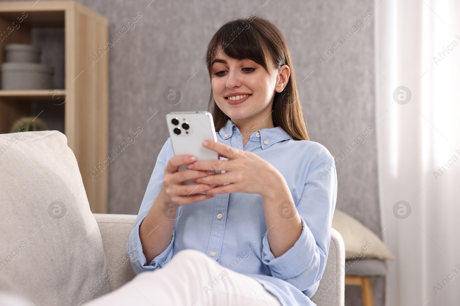 Photo of Beautiful young housewife using smartphone on sofa at home