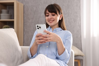 Beautiful young housewife using smartphone on sofa at home