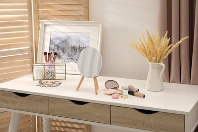 Photo of Dressing table with mirror, cosmetic products and jewelry in makeup room