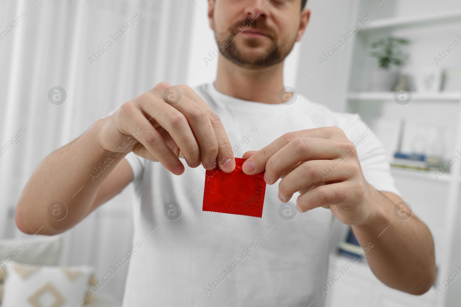 Photo of Closeup of man opening pack with condom indoors