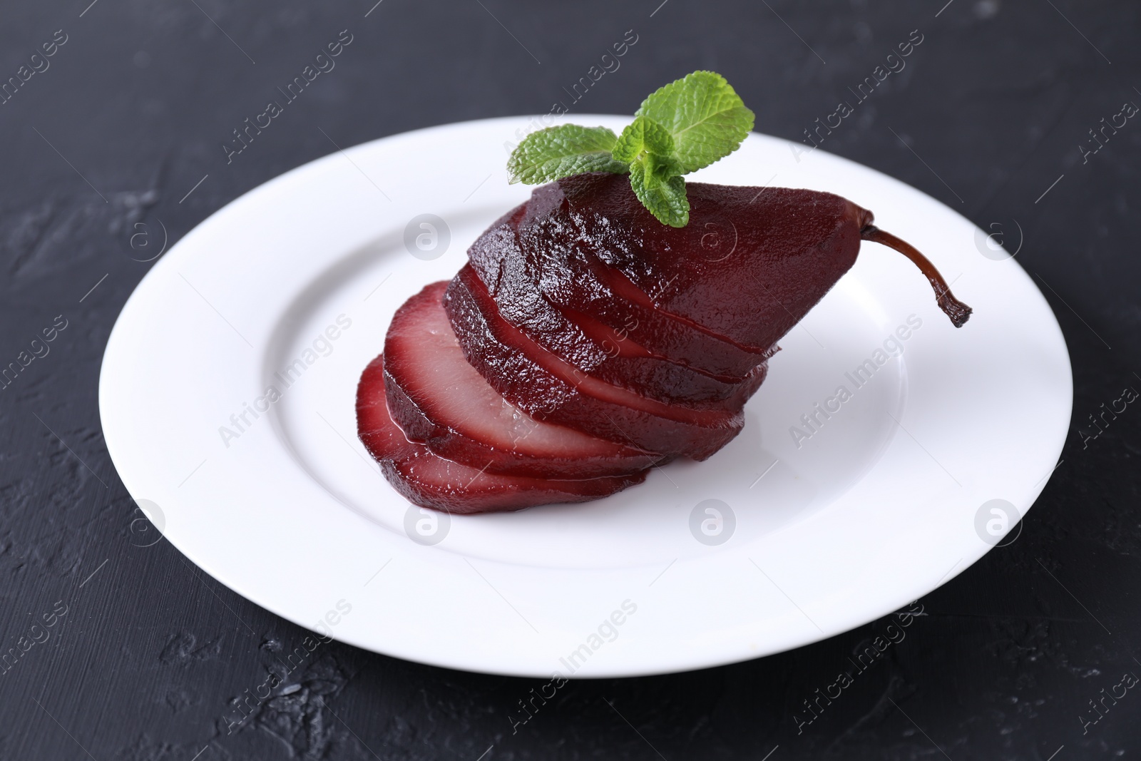 Photo of Tasty red wine poached pear and mint on black table, closeup