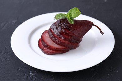 Tasty red wine poached pear and mint on black table, closeup