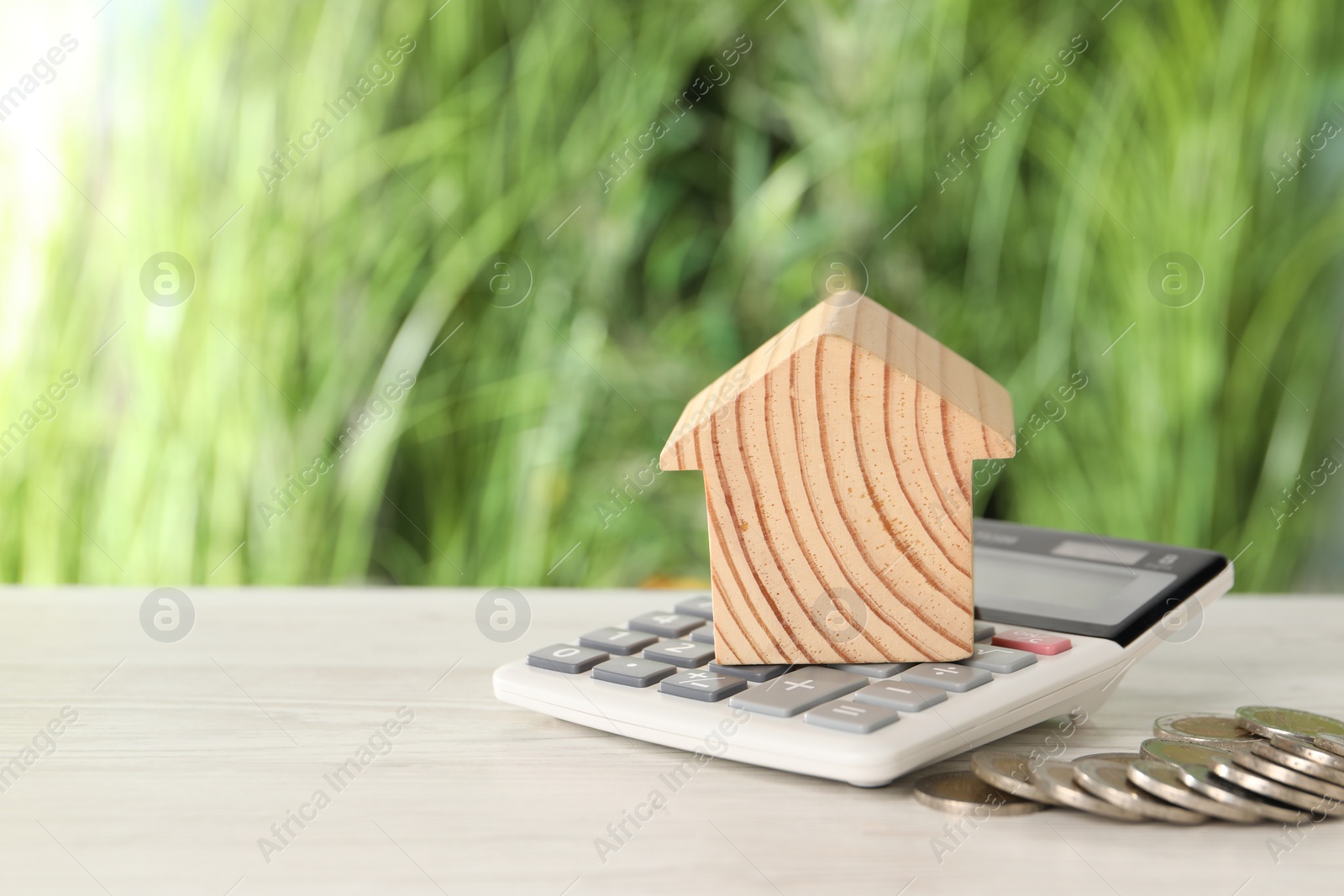 Photo of Wooden house model, calculator and coins on light table outdoors, space for text