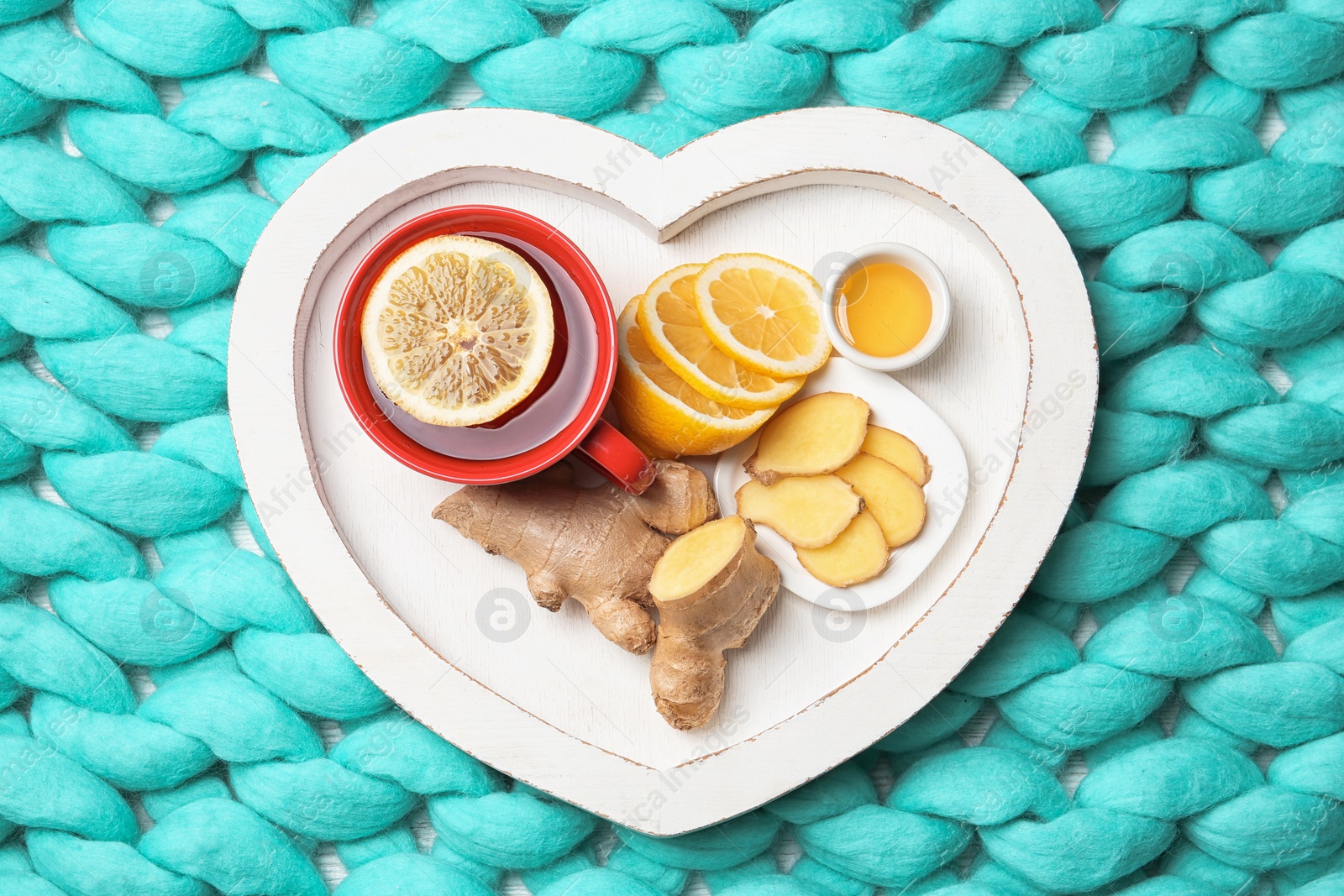 Photo of Heart shaped tray with lemon ginger tea on knitted background, flat lay