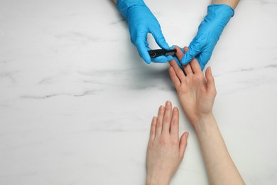 Photo of Diabetes. glucose testing. Doctor using lancet pen at white marble table, top view. Space for text