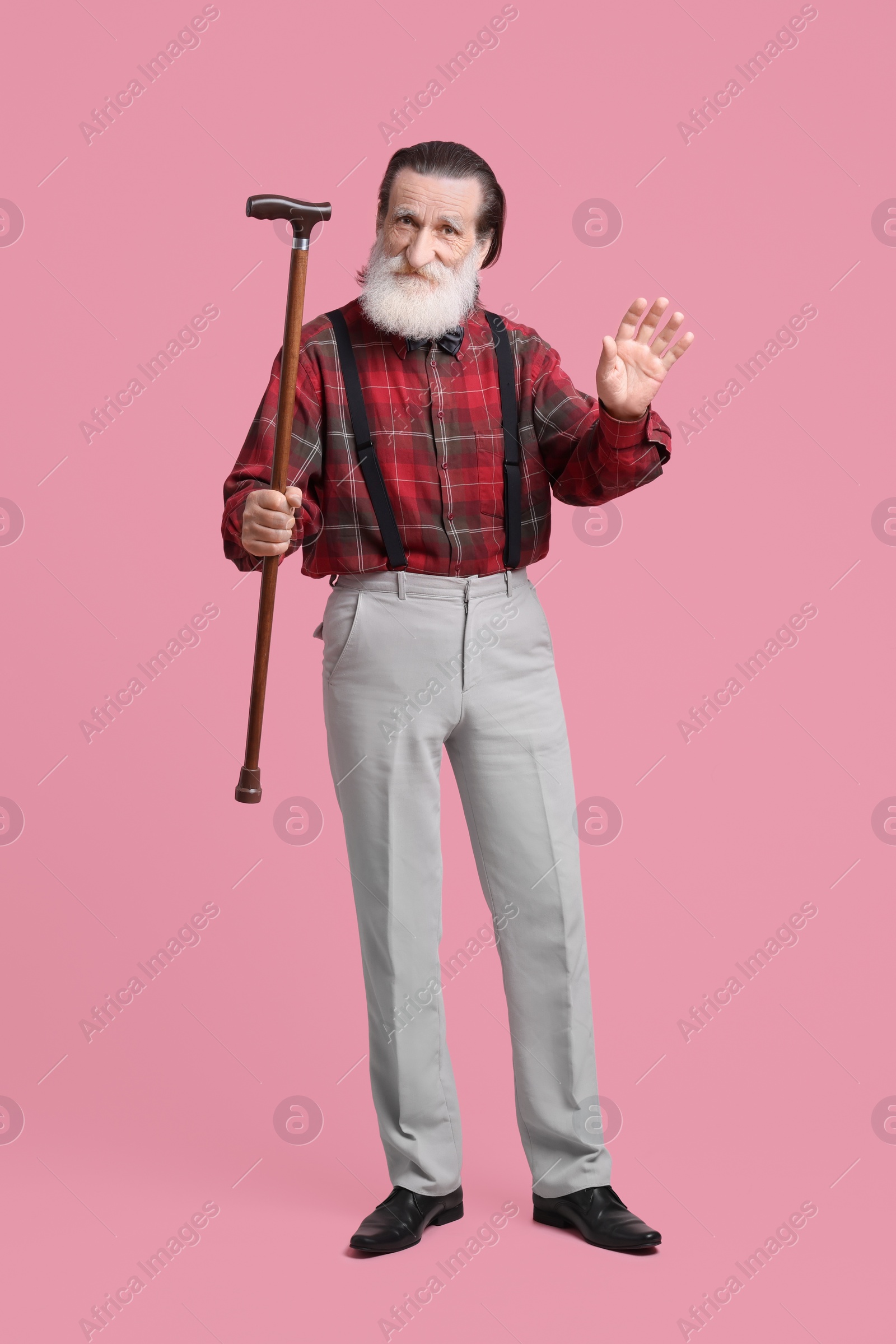 Photo of Senior man with walking cane waving on pink background