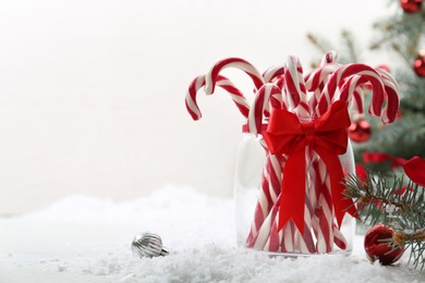 Photo of Candy canes in glass jar and Christmas balls on table against light background. Space for text