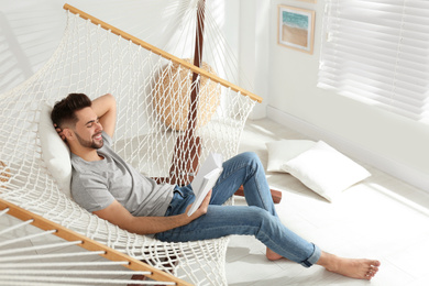 Photo of Young man reading book in hammock at home