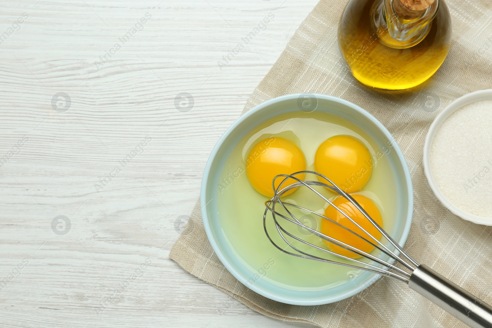 Photo of Whisking eggs in bowl on white wooden table, top view. Space for text