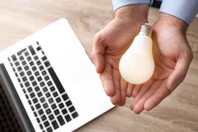 Photo of Man holding lamp bulb over table with laptop, top view