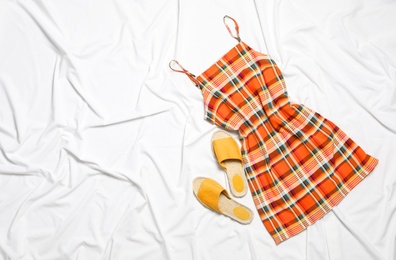 Stylish checkered dress and shoes on white fabric, flat lay. Space for text