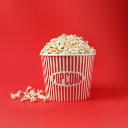 Photo of Delicious popcorn in paper bucket on red background