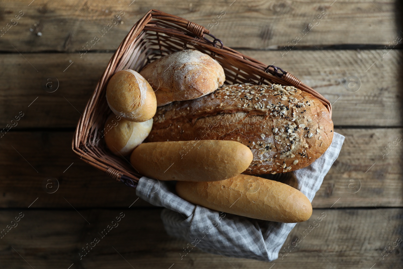 Photo of Wicker basket with different types of bread on wooden table, top view