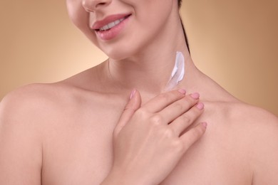 Photo of Woman with smear of body cream on her neck against light brown background, closeup