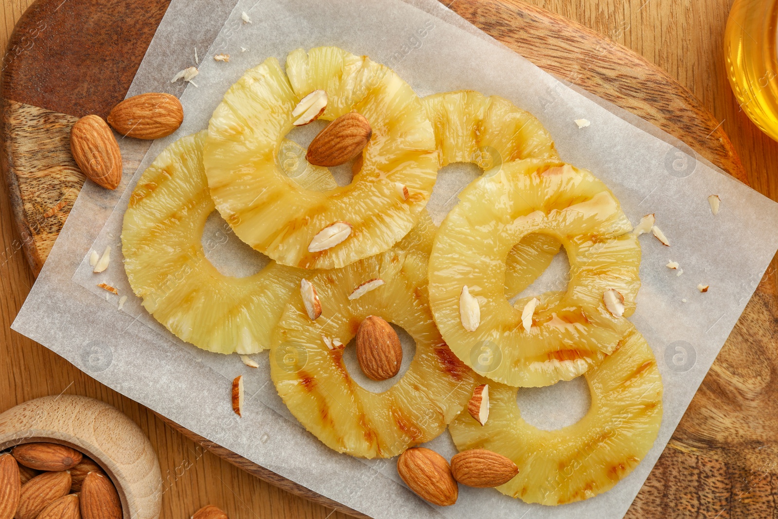 Photo of Tasty grilled pineapple slices and almonds on wooden table, flat lay