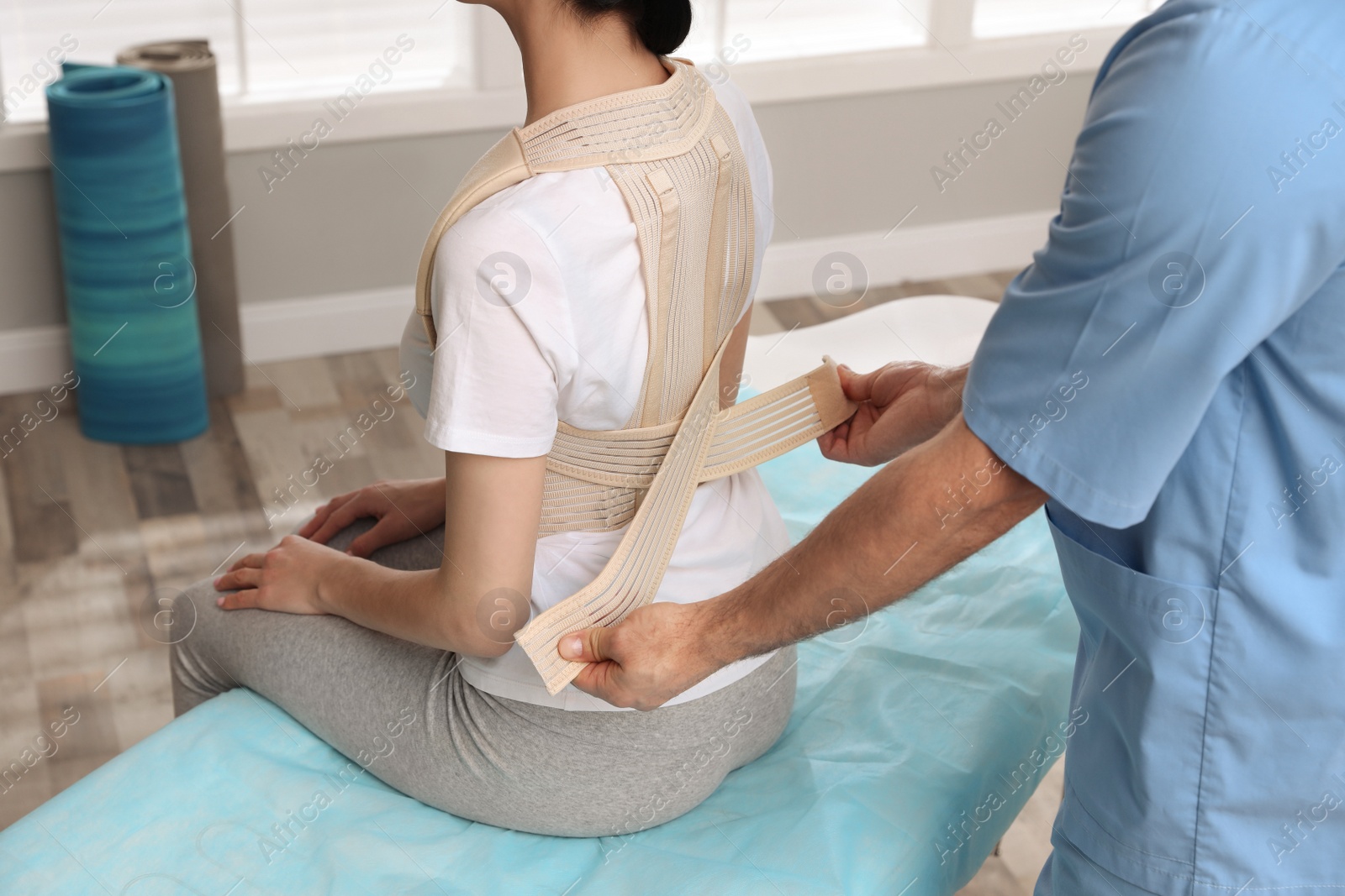 Photo of Orthopedist helping patient to put on posture corrector in clinic, closeup. Scoliosis treatment