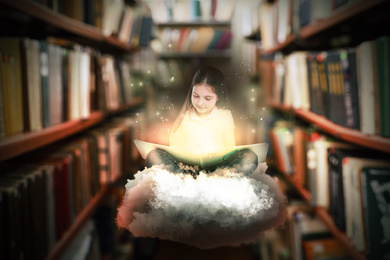 Image of Cute little girl reading magic book in library 