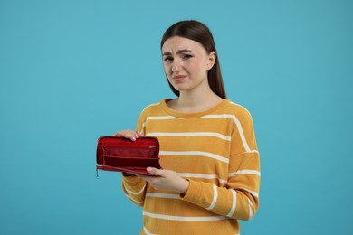 Sad woman showing empty wallet on light blue background