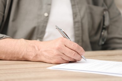 Senior man signing Last Will and Testament at wooden table, closeup