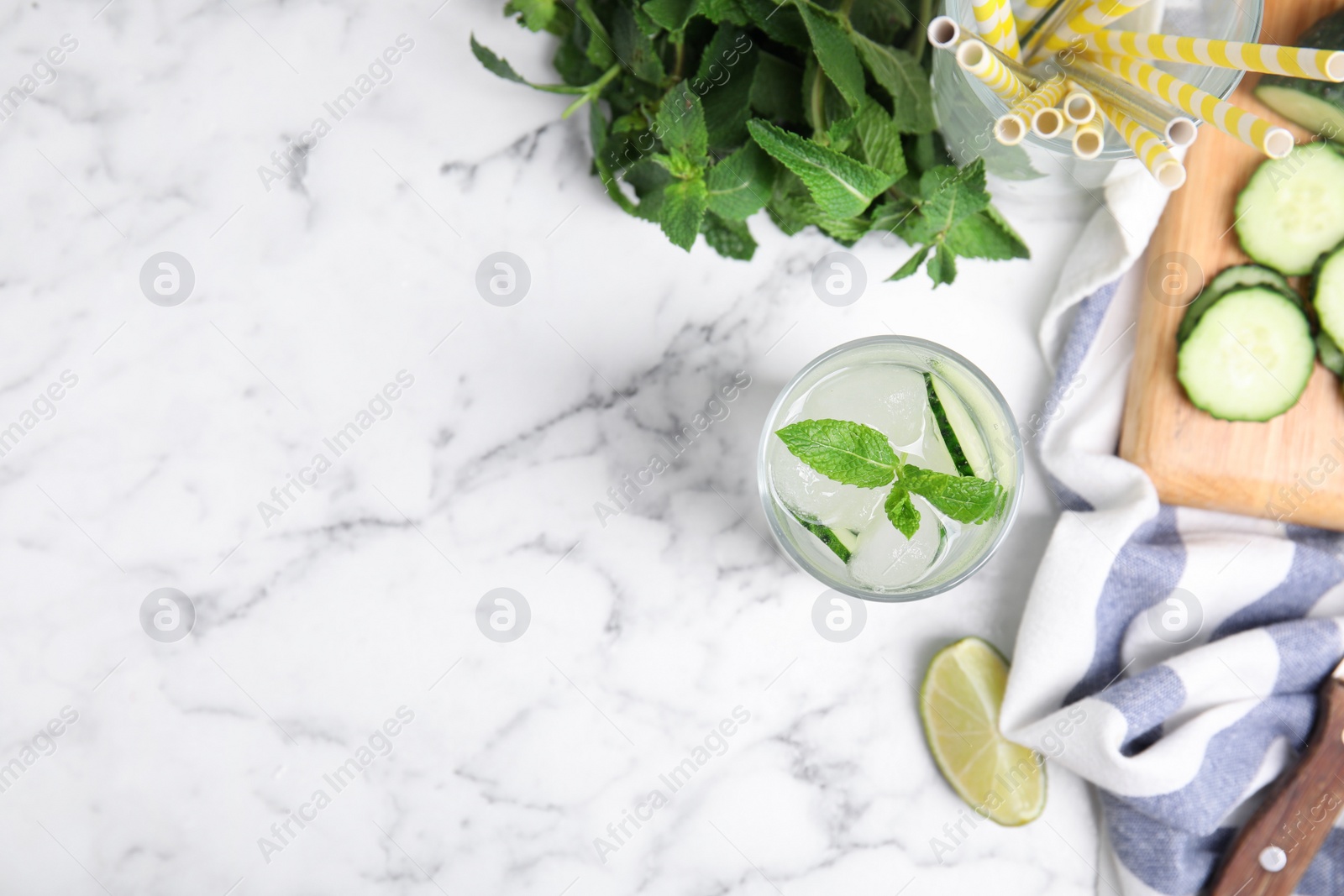 Photo of Glass of refreshing cucumber water and ingredients on white marble table, flat lay. Space for text