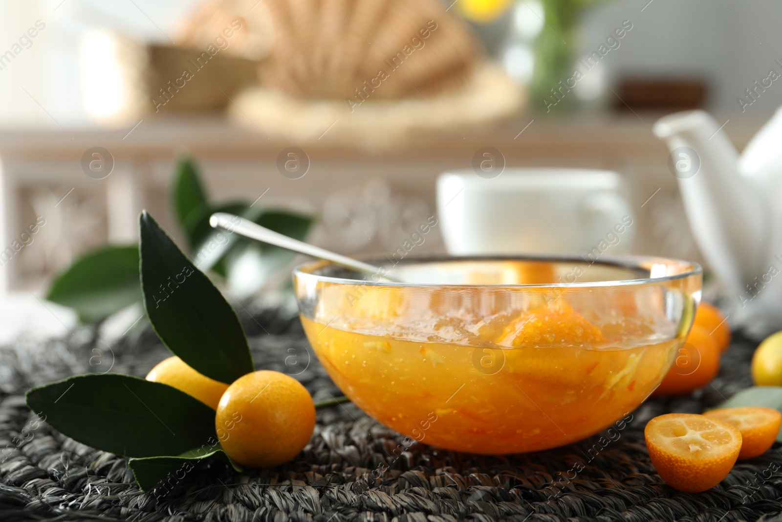 Photo of Delicious kumquat jam and fresh fruits on wicker mat, closeup