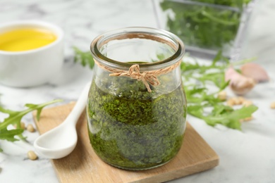 Photo of Jar of tasty arugula pesto and ingredients on white table