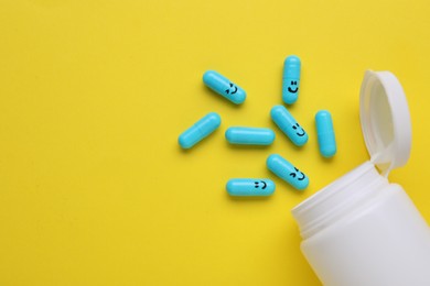 Photo of Colorful antidepressants with happy emoticons and medical bottle on yellow background, flat lay. Space for text