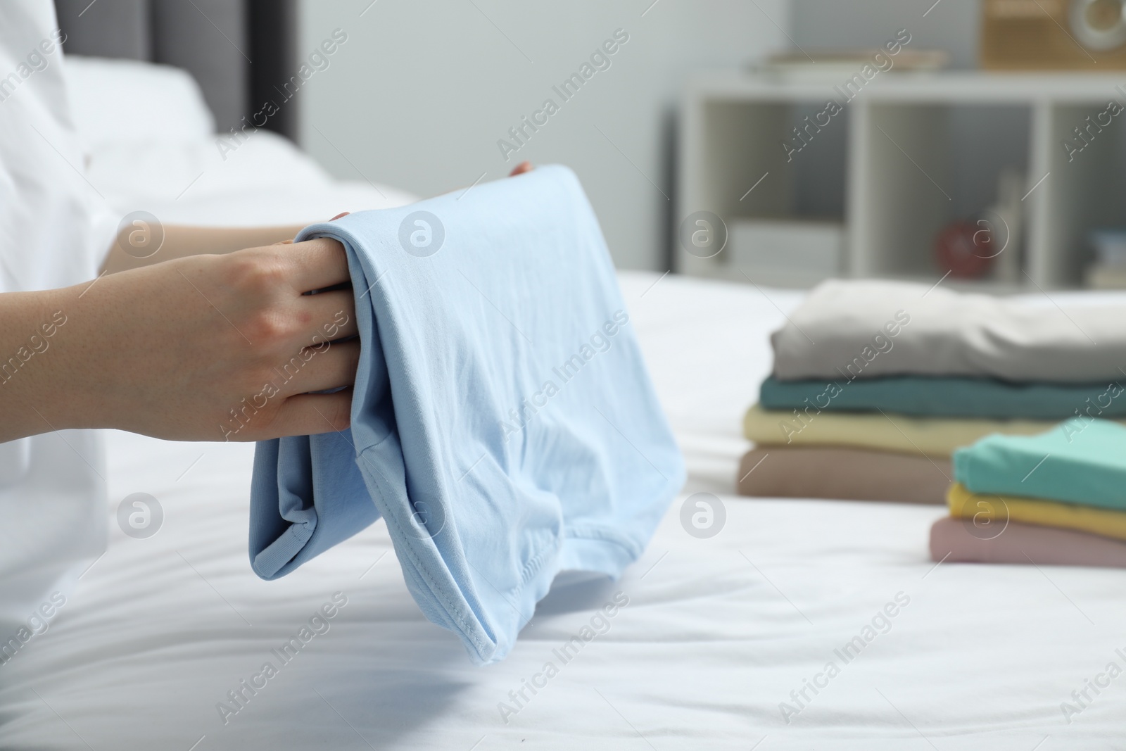 Photo of Woman folding clothes on bed indoors, closeup