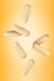 Image of Vitamin. Capsules falling on orange gradient background