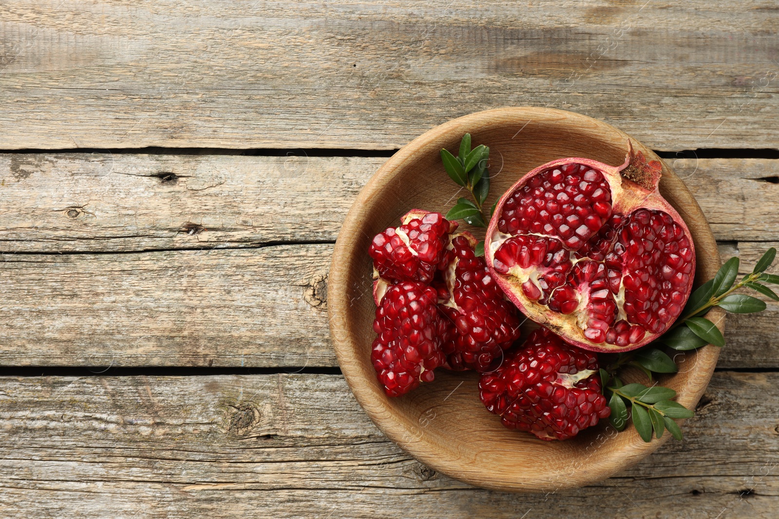 Photo of Cut fresh pomegranate and green leaves on wooden table, top view. Space for text