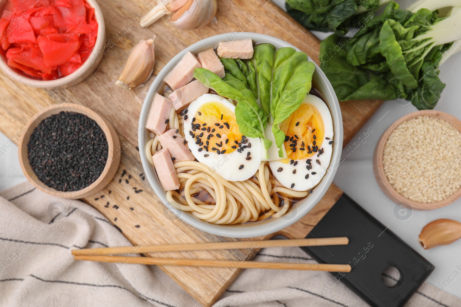 Photo of Bowl of delicious ramen with meat, egg and ingredients on white table, flat lay. Noodle soup