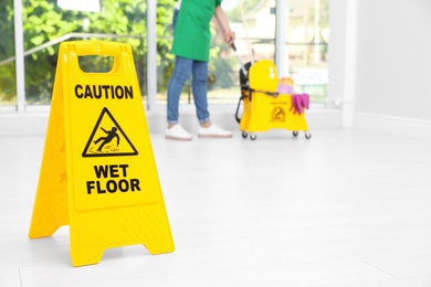 Photo of Safety sign with phrase "CAUTION WET FLOOR" and young woman cleaning, indoors