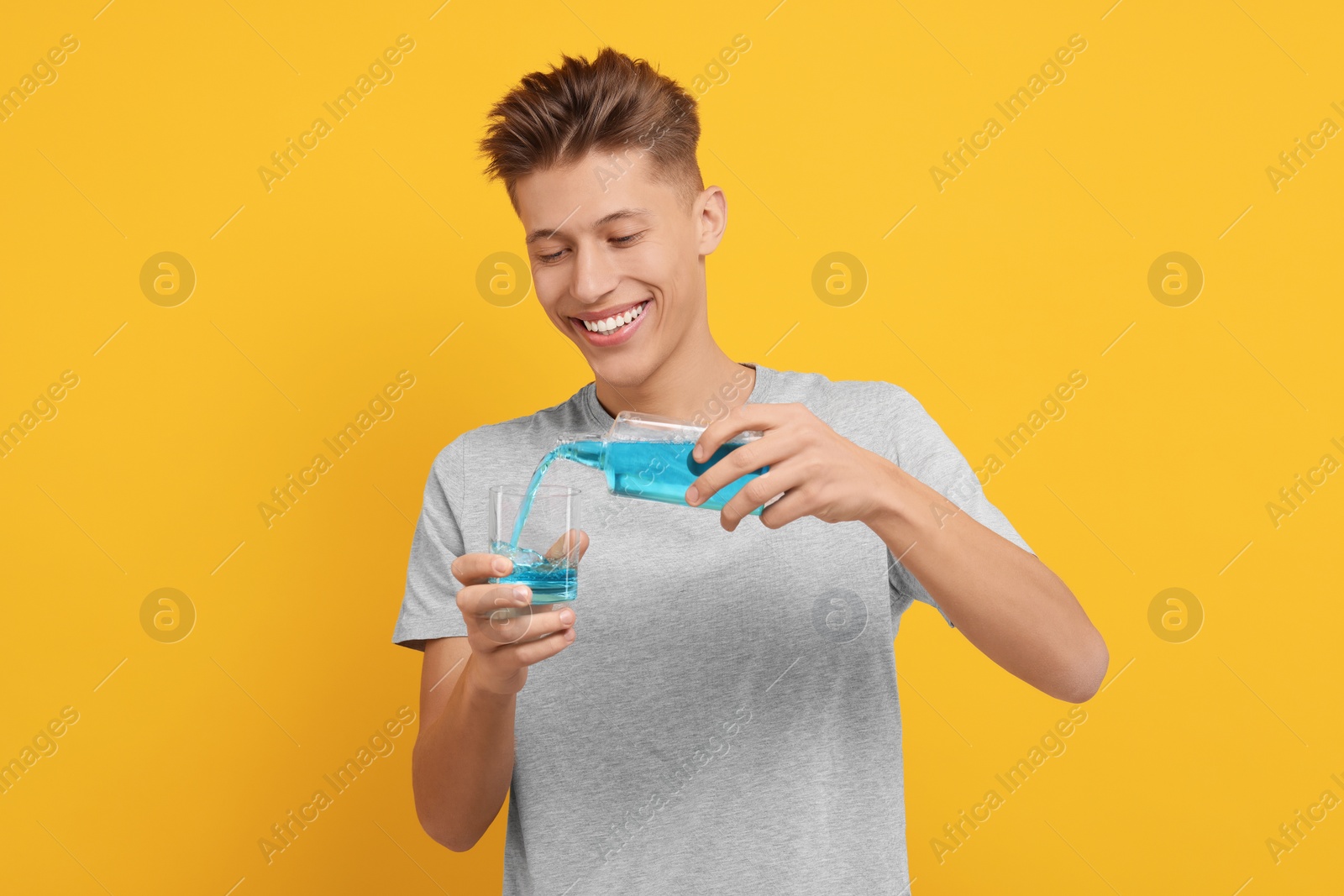 Photo of Young man using mouthwash on yellow background