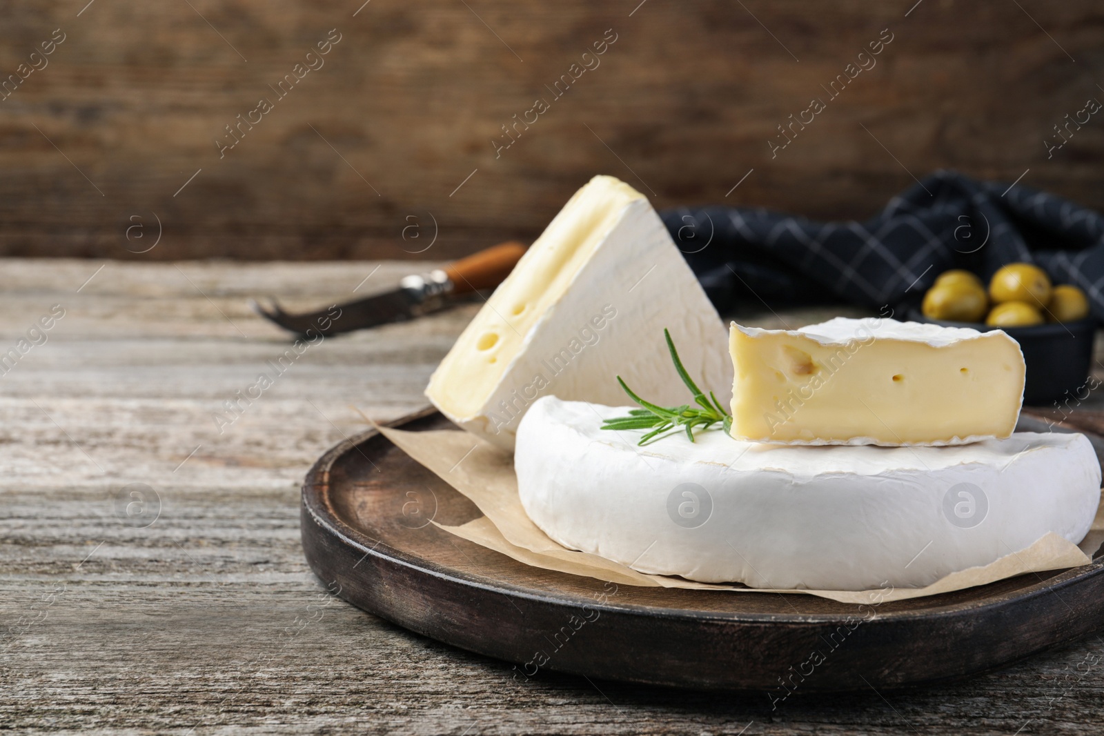 Photo of Tasty cut brie cheese with rosemary on wooden table, space for text