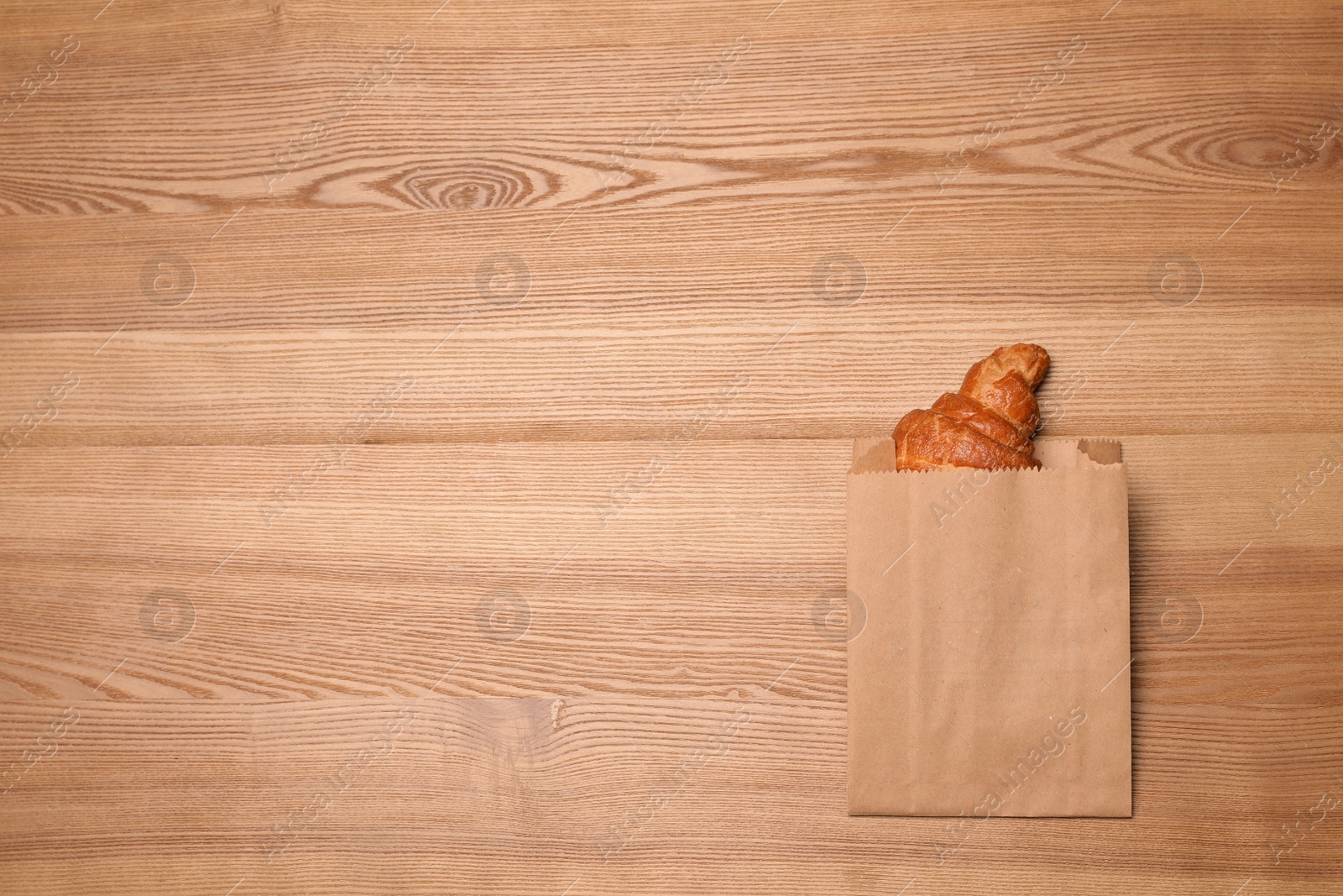 Photo of Paper bag with delicious croissant on wooden background, top view. Space for text