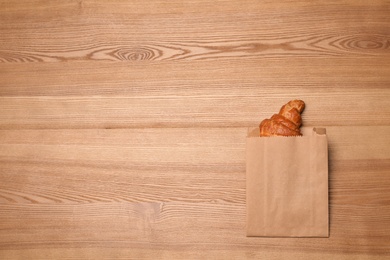 Paper bag with delicious croissant on wooden background, top view. Space for text