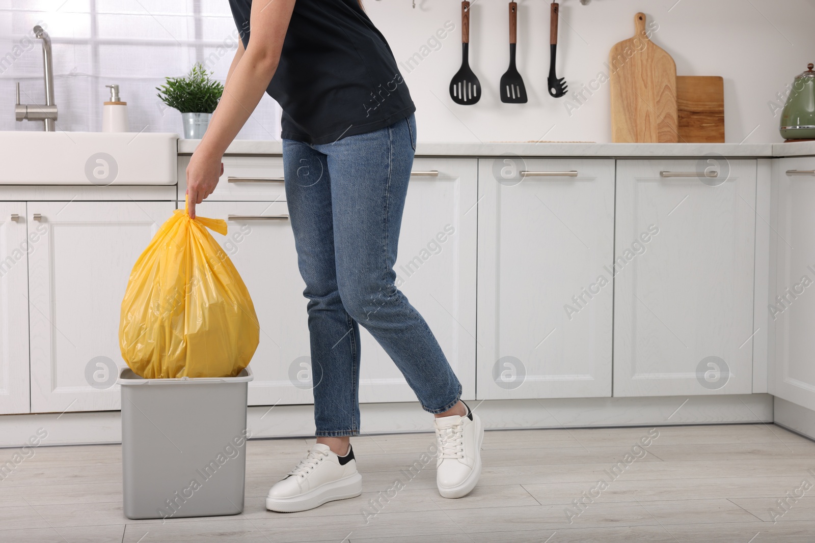 Photo of Woman taking garbage bag out of trash bin in kitchen, closeup. Space for text