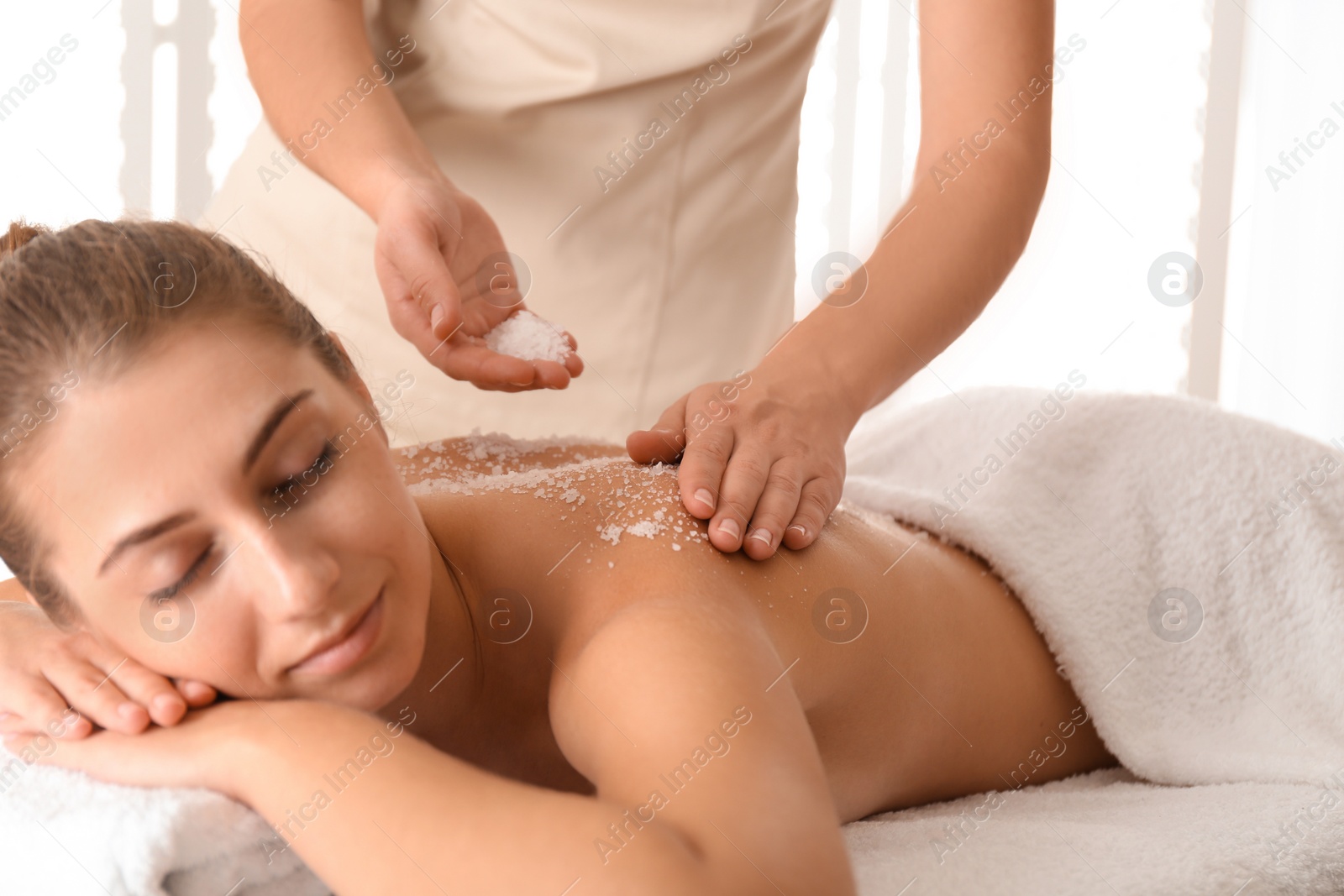 Photo of Young woman having body scrubbing procedure with sea salt in spa salon